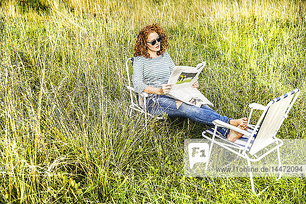 Junge Frau entspannt sich auf einer Wiese und liest Zeitung