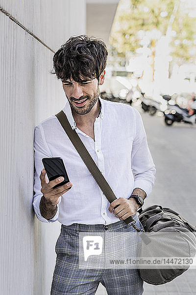 Junger Mann mit Tasche telefoniert mit seinem Handy in der Stadt