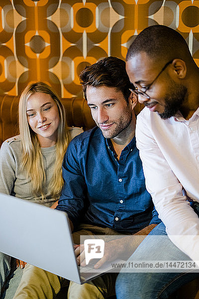 Three people sitting on couch in vintage living room sharing laptop