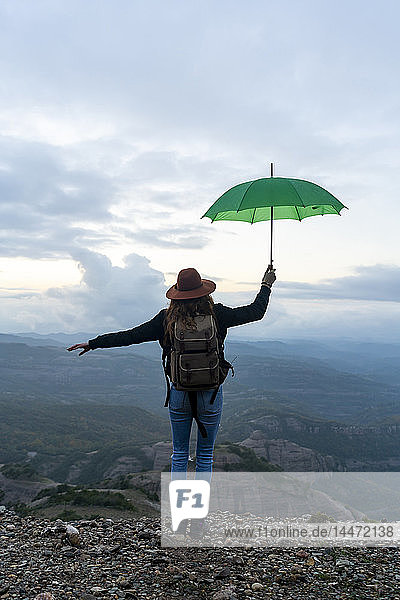 Woman standing on a mountain  looking at view  holding a green umbrella
