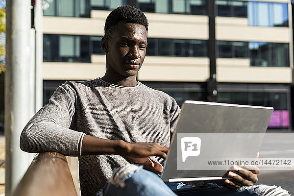 Young man sitting on a bench in the city  using laptop