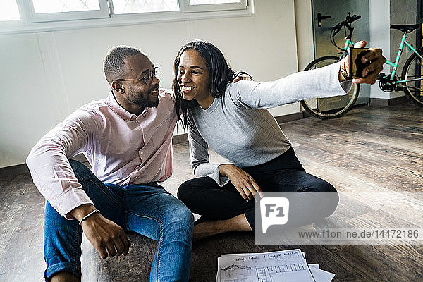 Smiling businessman and businesswoman sitting on the floor taking a selfie