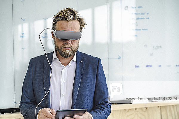 Geschäftsmann im Büro stehend  mit VR-Brille und digitalem Tablet