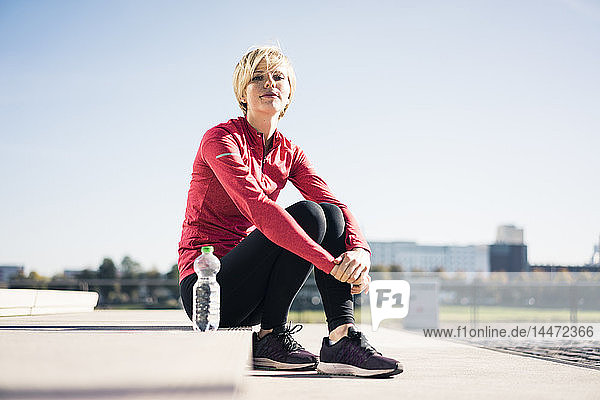 Young woman sitting at the riverside  taking a break after training