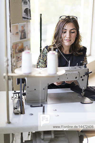 Porträt einer jungen Designerin  die in ihrem Atelier eine Nähmaschine benutzt