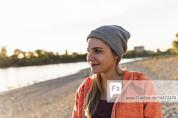 Porträt einer sportlichen jungen Frau am Fluss  die einen Mützenhut trägt