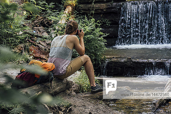 Rückansicht eines Wanderers im Wald beim Fotografieren eines Wasserfalls