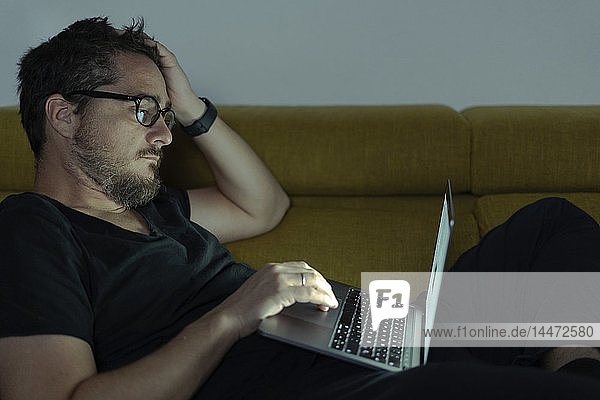 Man lying on couch using laptop at night
