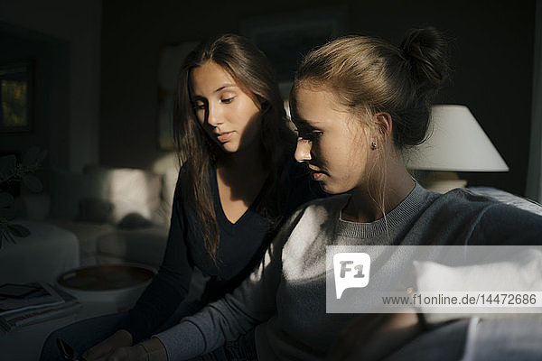 Two teenage girls using cell phone on couch at home