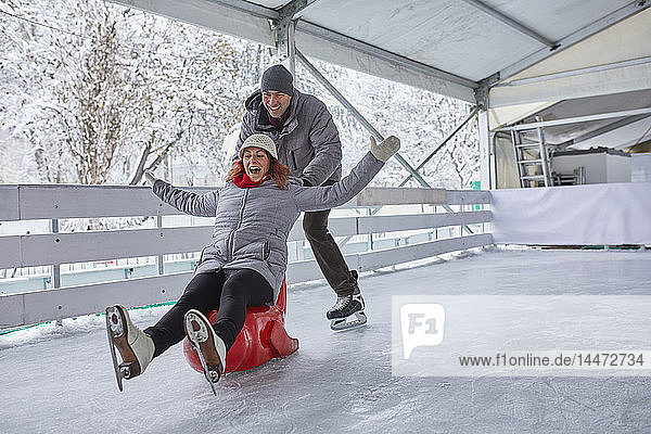 Couple ice skating  using seal sledge to push woman