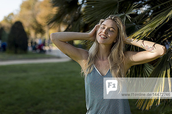 Porträt einer glücklichen jungen Frau an einer Palme im Park