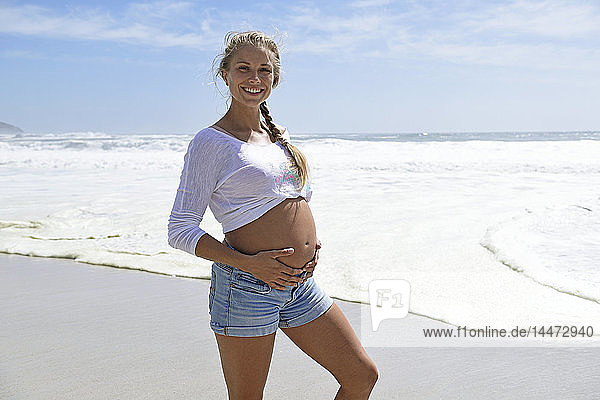 Porträt einer lächelnden schwangeren Frau am Strand