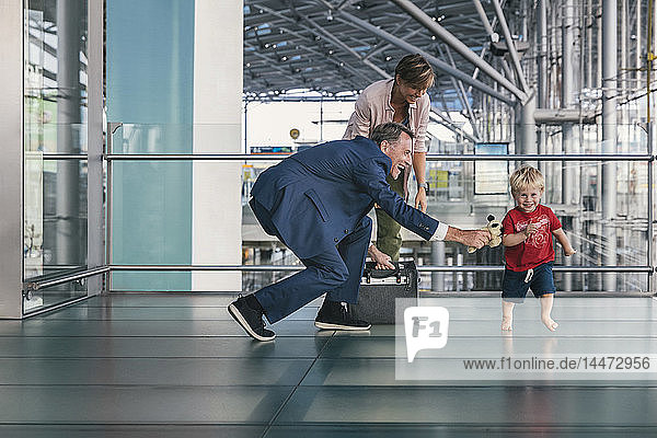 Happy child running around travelling businessman at the airport