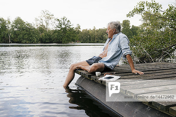 Älterer Mann sitzt auf einem Steg an einem See