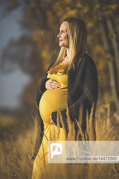 Lächelnde schwangere Frau steht im Herbst in der Natur