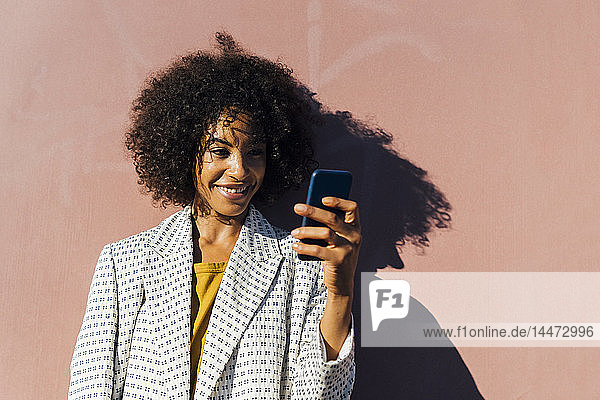 Schöne Frau steht vor der Wand und fotografiert mit ihrem Smartphone
