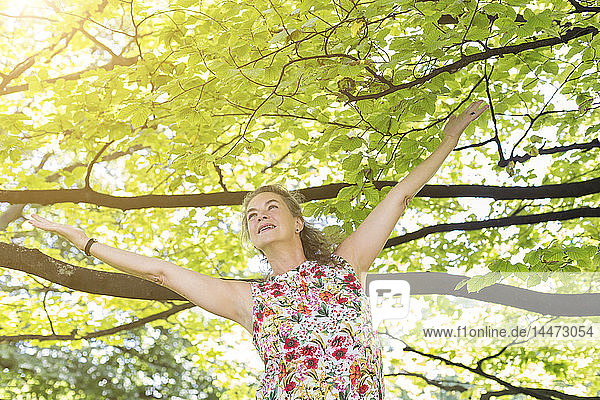 Lächelnde reife Frau  die ein Top mit Blumendesign trägt und sich in einem Park entspannt