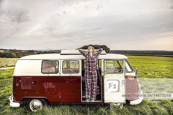 Woman in pyjama stretching in a van in rural landscape