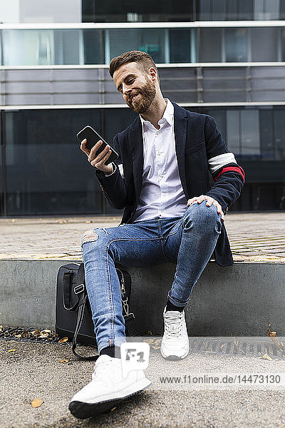 Stilvoller Geschäftsmann sitzt in der Stadt und benutzt sein Handy