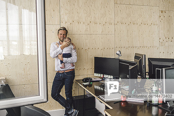 Working father standing in office  holding his son