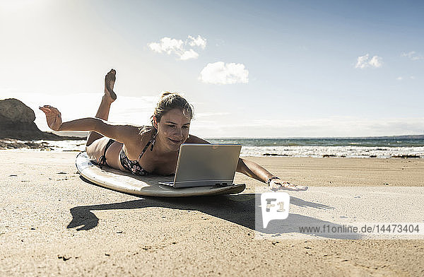 Junge Frau liegt auf einem Surfbrett und benutzt einen Laptop