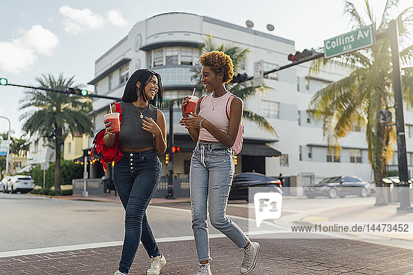 USA  Florida  Miami Beach  zwei glückliche Freundinnen bei einem Erfrischungsgetränk über die Straße