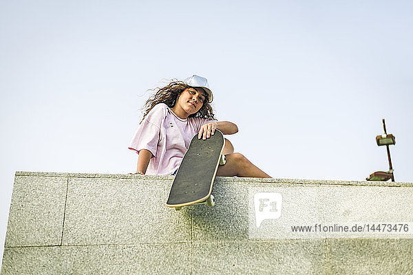 Mädchen mit Skateboard an der Wand sitzend