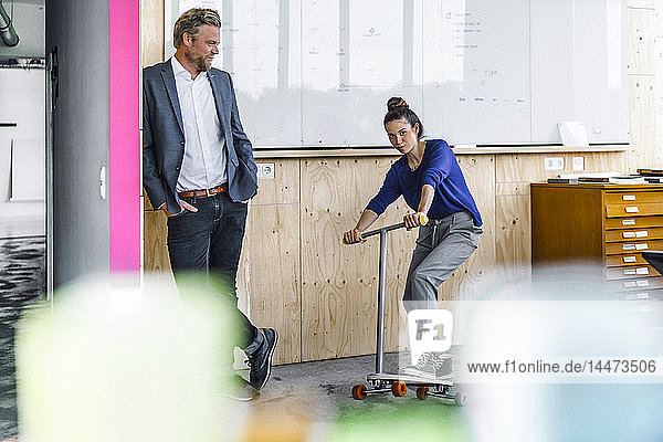 Mature man and his assistent playing with scooter  standing in office in front of white board