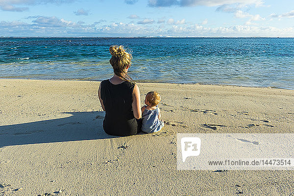 Cook-Inseln  Rarotonga  Frau sitzt mit ihrem Baby an einem weißen Sandstrand