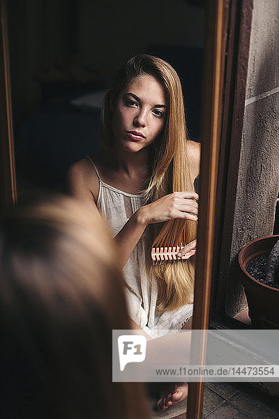 Spiegelbild einer jungen Frau  die sich selbst beim Kämmen beobachtet