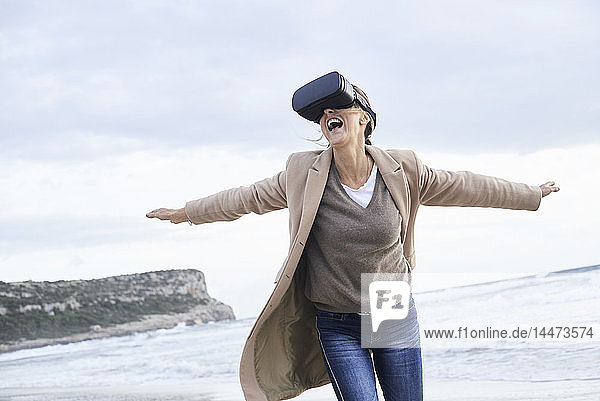 Spain  Menorca  senior woman using VR glasses on the beach in winter