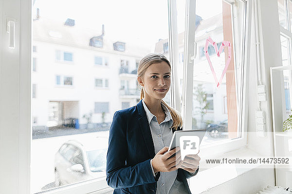 Junge Geschäftsfrau steht am Fenster und benutzt ein digitales Tablet