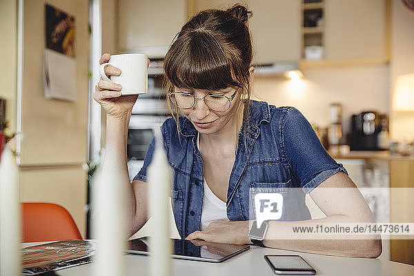 Frau sitzt mit einer Tasse Kaffee am Tisch in der Küche und benutzt Tabletten
