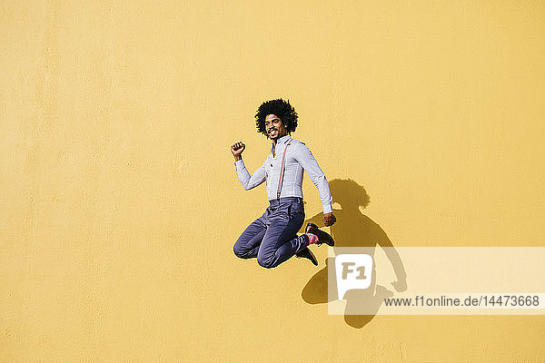 Lächelnder Mann springt vor gelber Mauer in die Luft