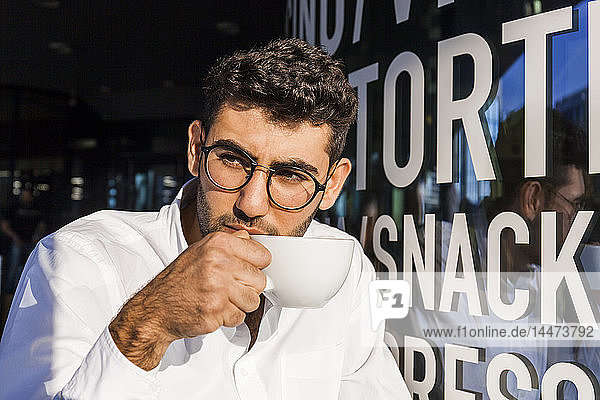 Porträt eines jungen Geschäftsmannes  der im Straßencafé Kaffee trinkt und etwas beobachtet