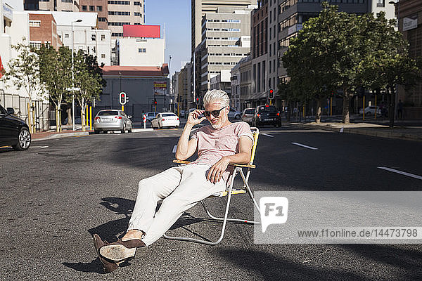 Mature man sitting on chair in the street  wearing sunglasses