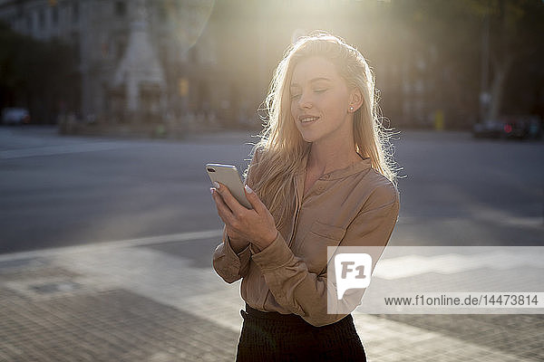 Lächelnde junge Geschäftsfrau benutzt Mobiltelefon in der Stadt