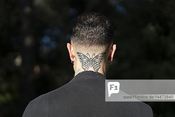 Rückenansicht eines Mannes mit tätowiertem Schmetterling am Hals
