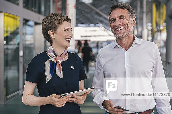 Happy airline employee with tablet and passenger with cell phone at the airport