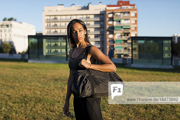 Sporty young woman with bag standing on meadow the city