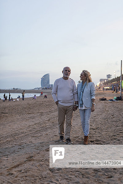Spanien  Barcelona  Seniorenpaar geht Hand in Hand in der Abenddämmerung am Strand