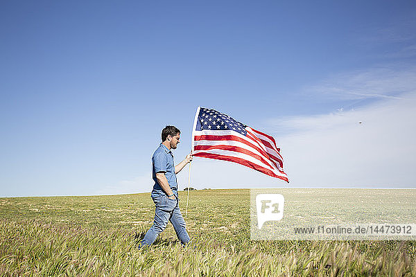 Man with American flag walking on field in remote landscape