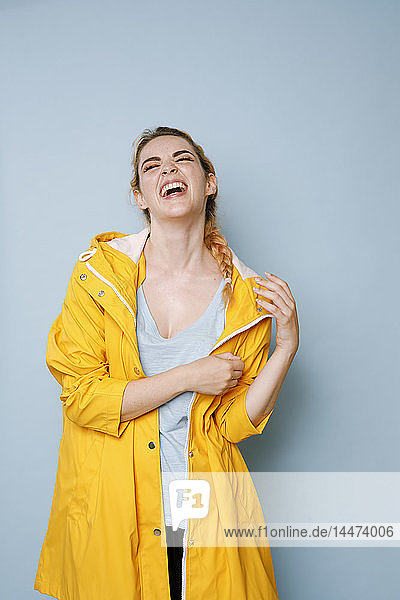 Porträt einer lachenden jungen Frau in gelbem Regenmantel vor blauem Hintergrund