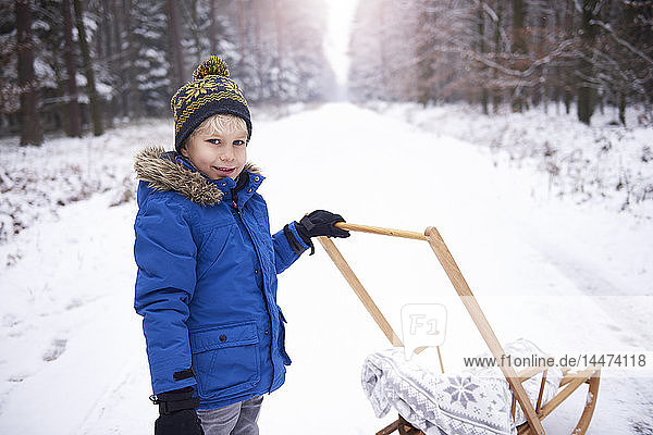 Portrait of smiling little boy with sledge in winter forest