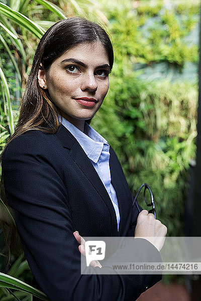 Porträt einer selbstbewussten jungen Geschäftsfrau umgeben von Pflanzen