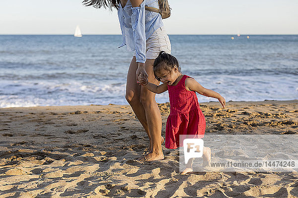 Mutter und kleine Tochter gehen am Strand spazieren und halten sich an den Händen