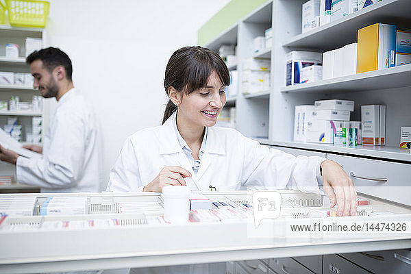 Smiling pharmacist seeking out medicine at cabinet in pharmacy