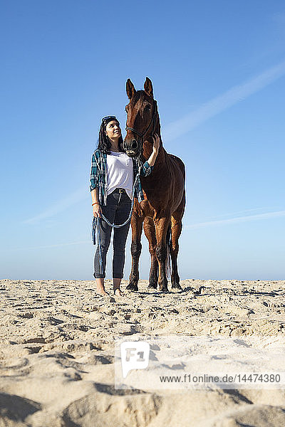 Woman with horse standing in sand