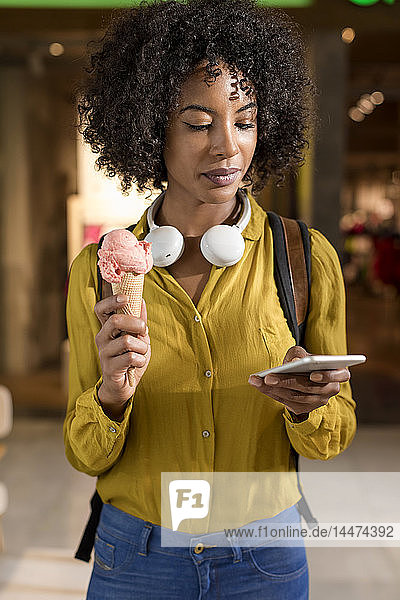Porträt einer Frau mit Eistüte  die auf ihr Handy schaut