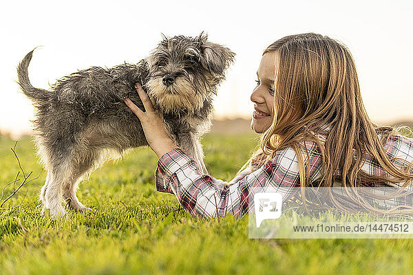 Lächelndes Mädchen liegt auf einer Wiese und spielt mit Hund
